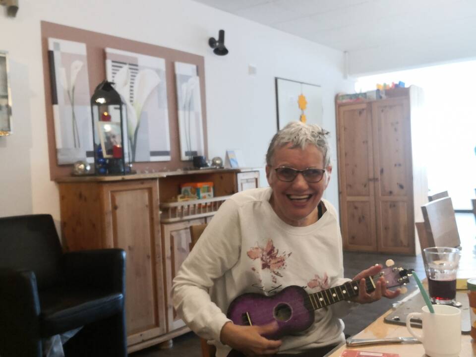 Eine Frau sitzt am Tisch mit einer Ukulele in den Händen.