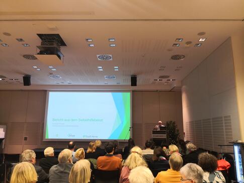 Menschen sitzen Richtung Leinwand in einem Raum.