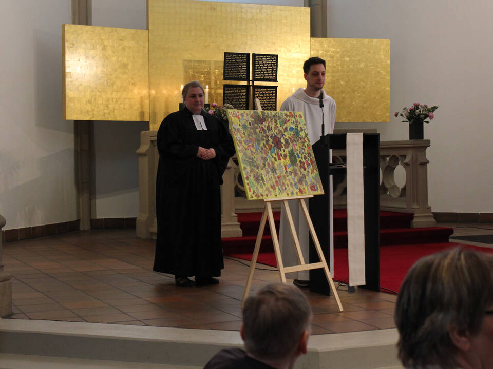 Der Pfarrer und ein Messdiener stehen hinter dem bunten Bild.