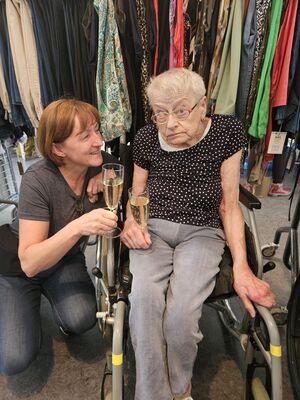 Eine Frau mit Sekt in der Hand schaut zu einer Frau die im Rollstuhl sitzt.