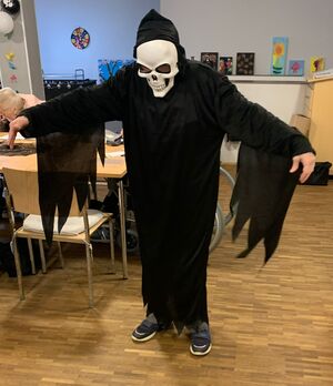 Eine Person in einem schwarzen Gewand und einer weißen Gesichtsmaske in einem Raum.