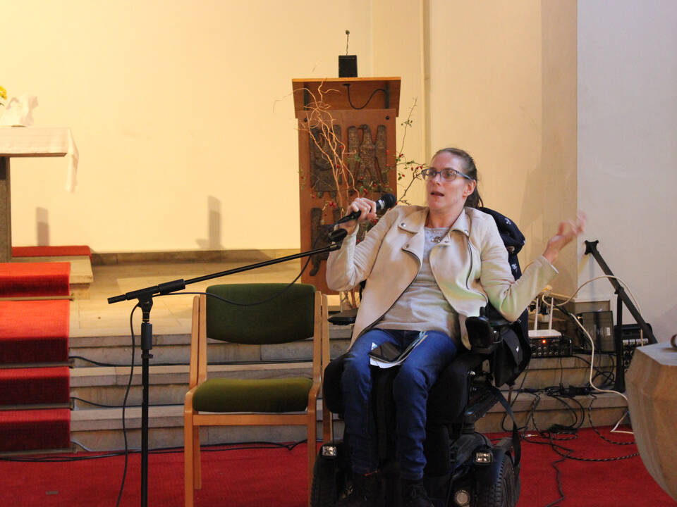 Eine Person im Rollstuhl hält ein Mikrofon in der Hand.