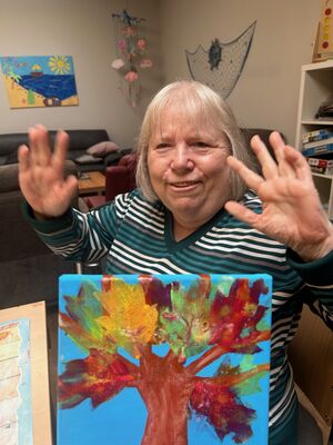 Eine Frau streckt die Hände in die Luft, vor ihr ein Bild mit einem Baum.