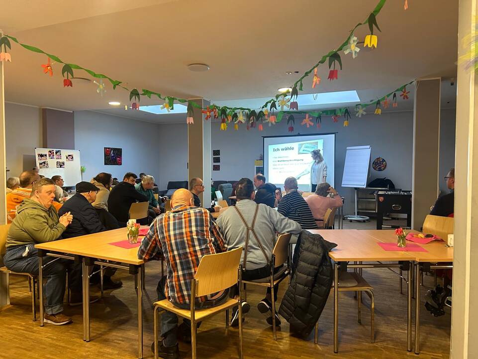 Viele Gäste auf einer Veranstaltung in einem großen Raum, vorne steht Anna Schnau.