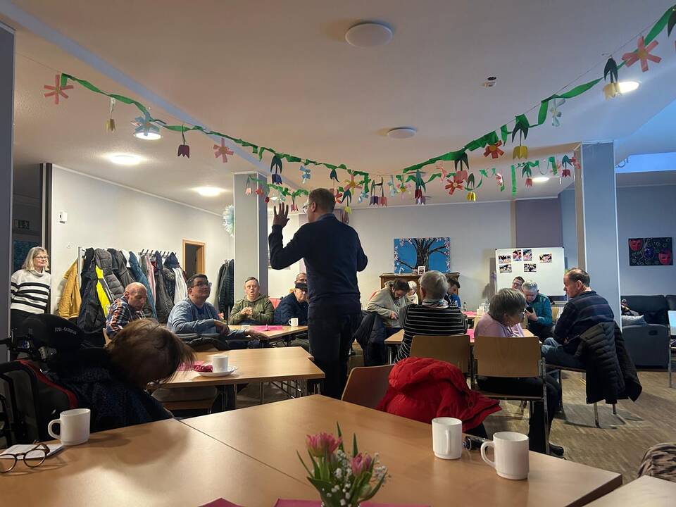 Ein Mann spricht mit den Gästen und hebt die Hände hoch.