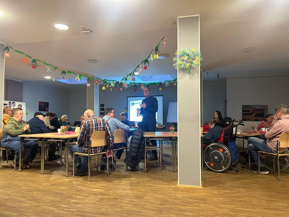 Ein Mann steht vor den Gästen und redet.