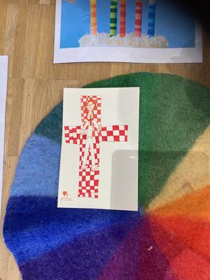 Ein Blatt mit einem Kreuz liegt auf einem Teppich mit Regenbogenfarben.