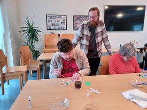 Personen sitzen am Tisch, ein Mann steht dahinter.