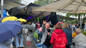 Viele Personen mit Regenschirmen stehen vor einer Bühne.