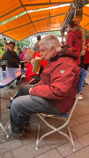 Ein Mann sitzt auf einem blauen Stuhl und trinkt ein Bier.