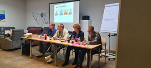 Die Politiker sitzen vor einer Leinwand an Tischen.