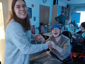 Eine junge Frau hält die Hände eines Rollstuhlfahrers in die Luft und lächelt.