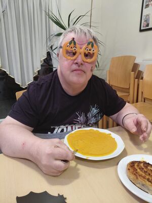 Ein Mann mit einer bunten Brille sitz am Tisch und hat den Löffel in einer Kürbisssuppe.