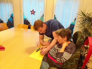 EIn MAnn hilft einer Person im Rollstuhl zu basteln.