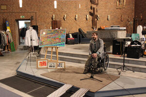 Eine Person im Rollstuhl steht neben Bildern.