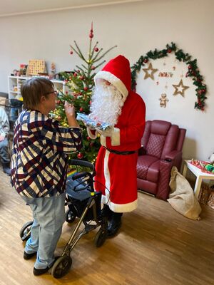 Der Nikolaus bei einer Person mit Rollator neben einem Weihnachtsbaum.