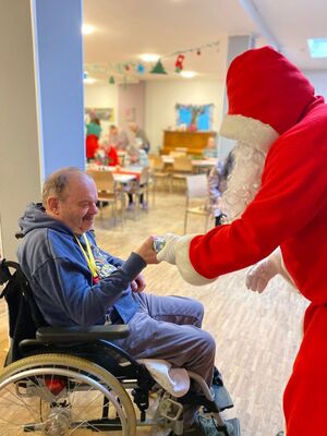 Der Nikolaus gibt einem Mann im Rollstuhl etwas.