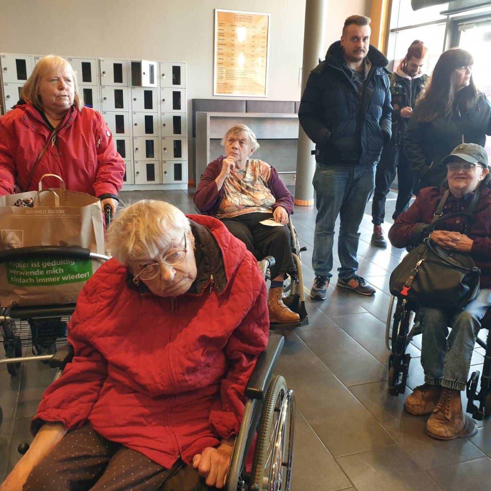 Einige Menschen mit Hilfmittel im Eingangsbereich.