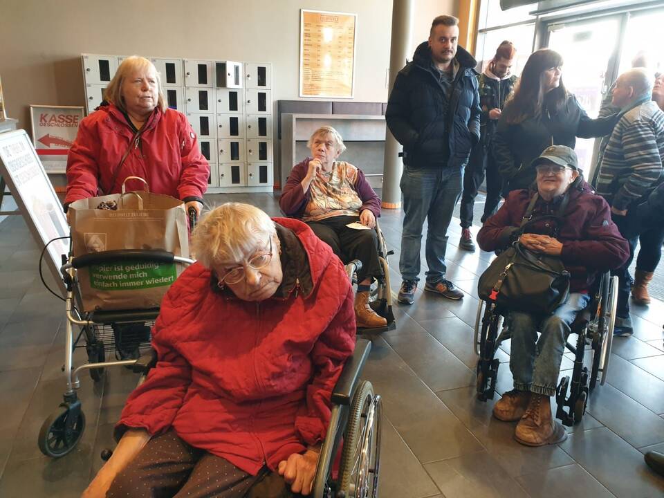 Einige Menschen mit Hilfmittel im Eingangsbereich.