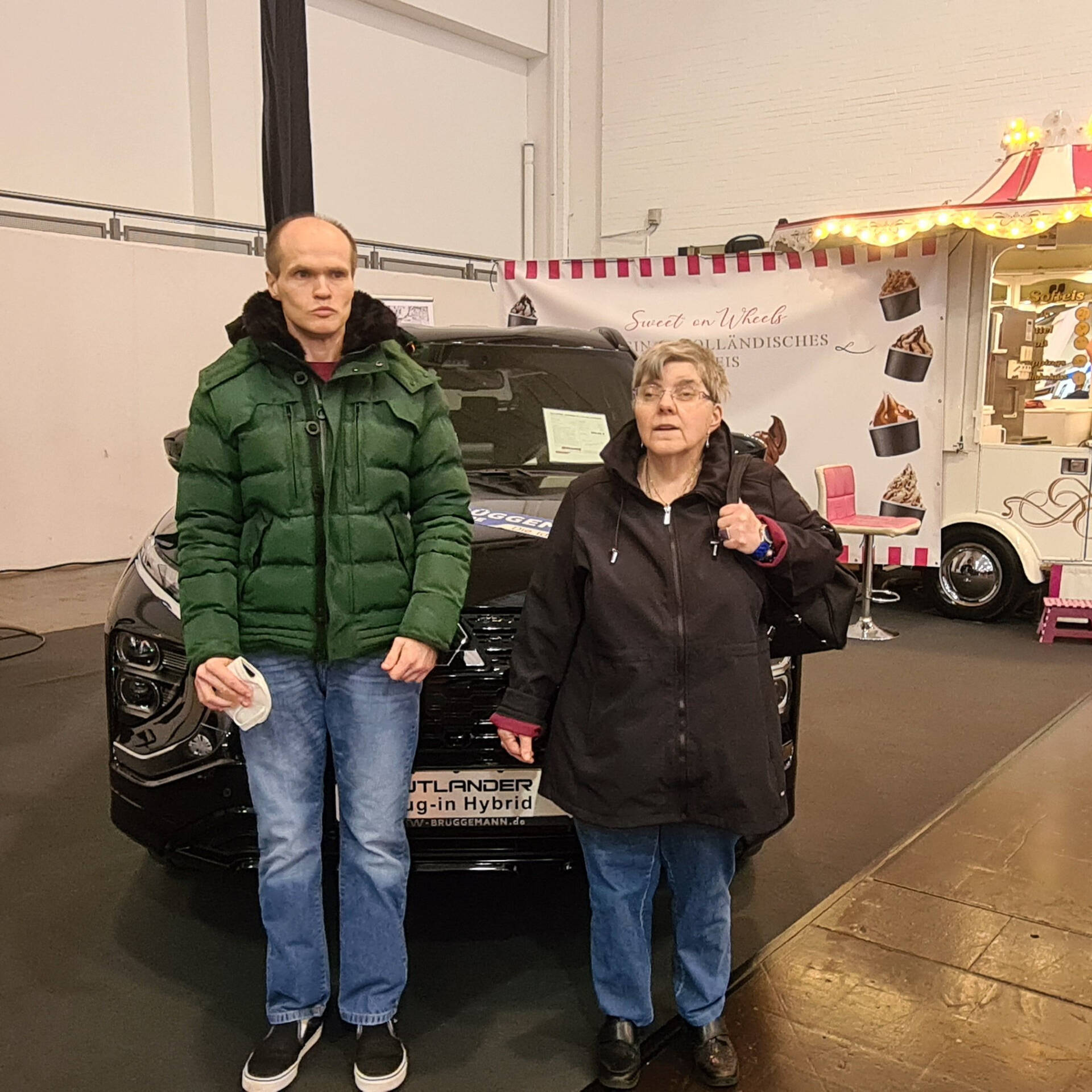 Zwei Personen stehen in einer Halle vor einem dunklen Auto.