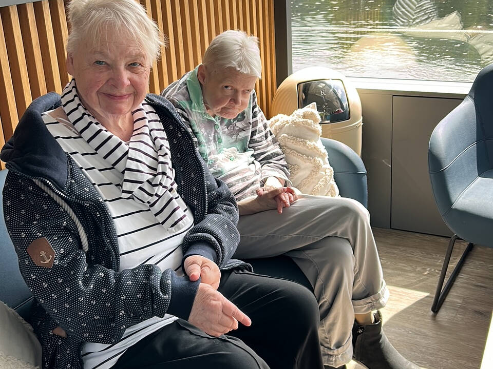 Zwei Personen sitzen an Deck im Schatten.