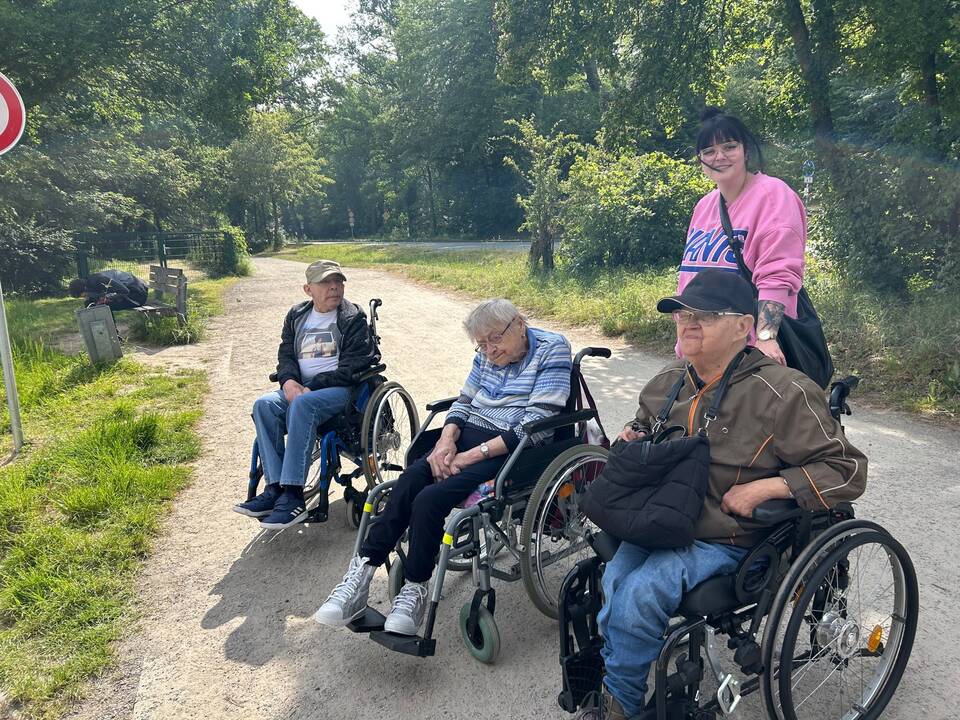 Drei Personen im Rollstuhl und eine steht dahinter.