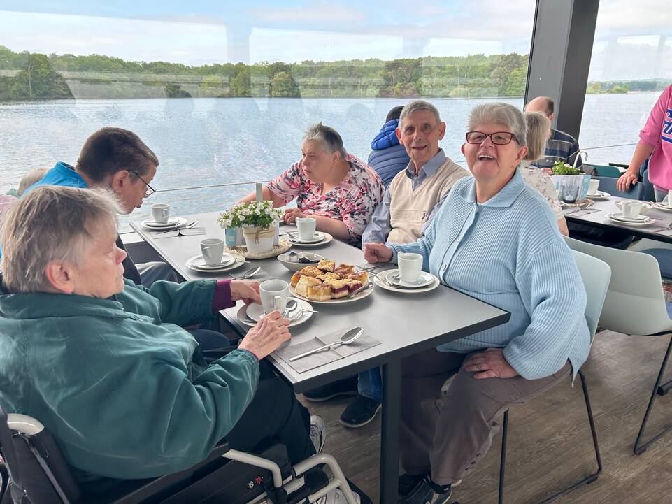 Sechs Personen sitzen am gedeckten Tisch mit Kuchen.