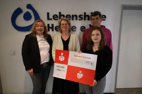Vier Personen mit einem Spendenscheck vor einem Lebenhilfe Schriftzug
