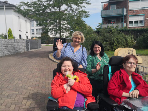 Zwei Frauen stehen hinter zwei Frauen im Rollstuhl, alle lachen.