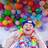 Eine Frau im Rollstuhl vor einer Wand mit bunten Luftballons.