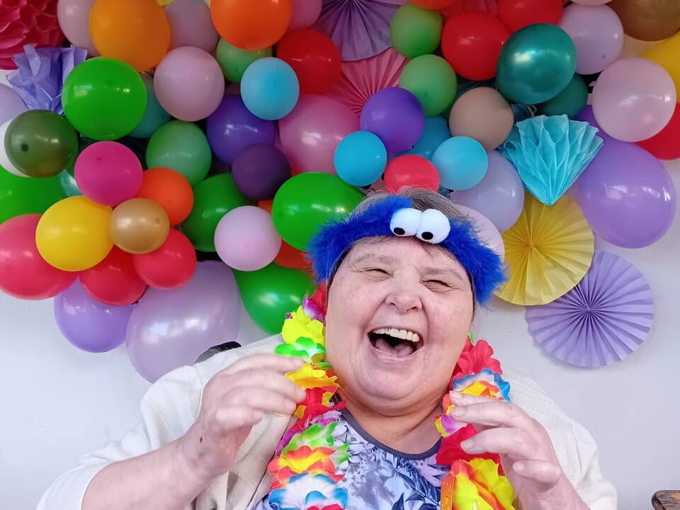 Eine Frau im Rollstuhl vor einer Wand mit bunten Luftballons.